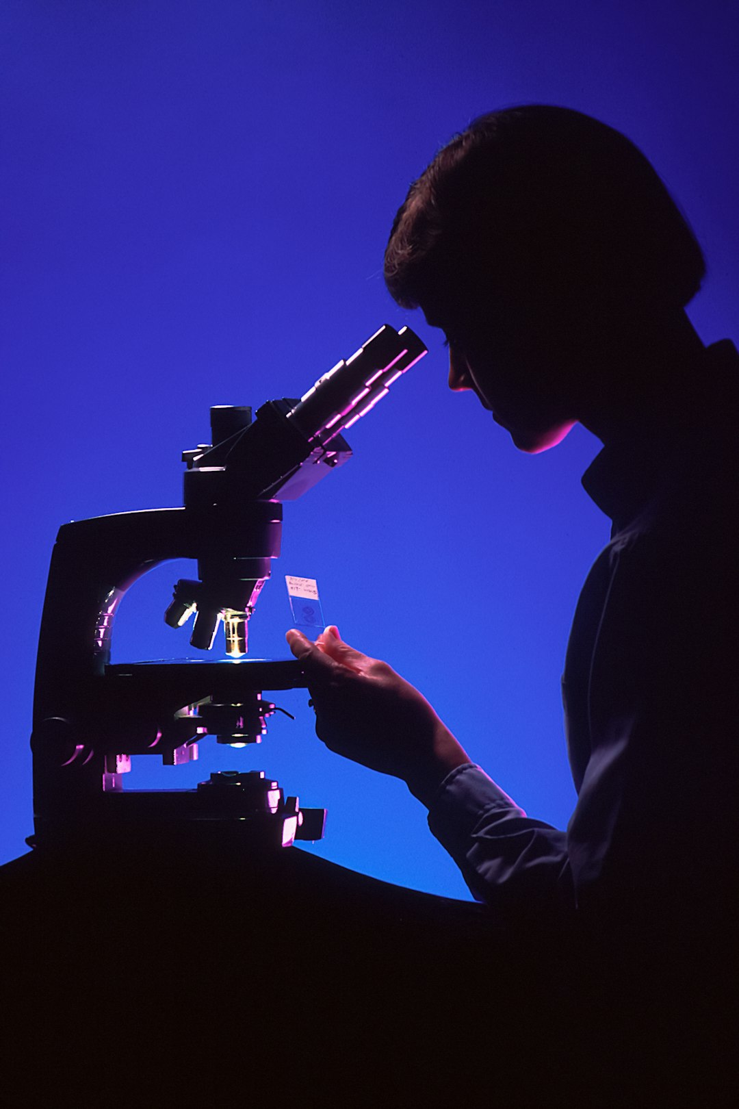 Silhueta de uma cientista ao microscópio em contraluz